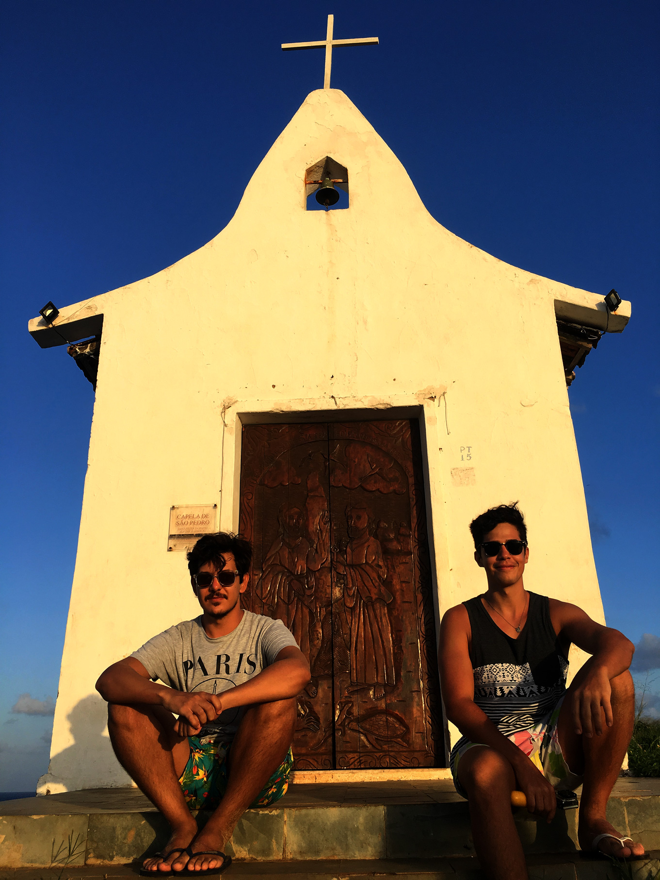 Henrique e Rodrigo sentados nos degraus da pequena capela de São Pedro dos Pescadores.