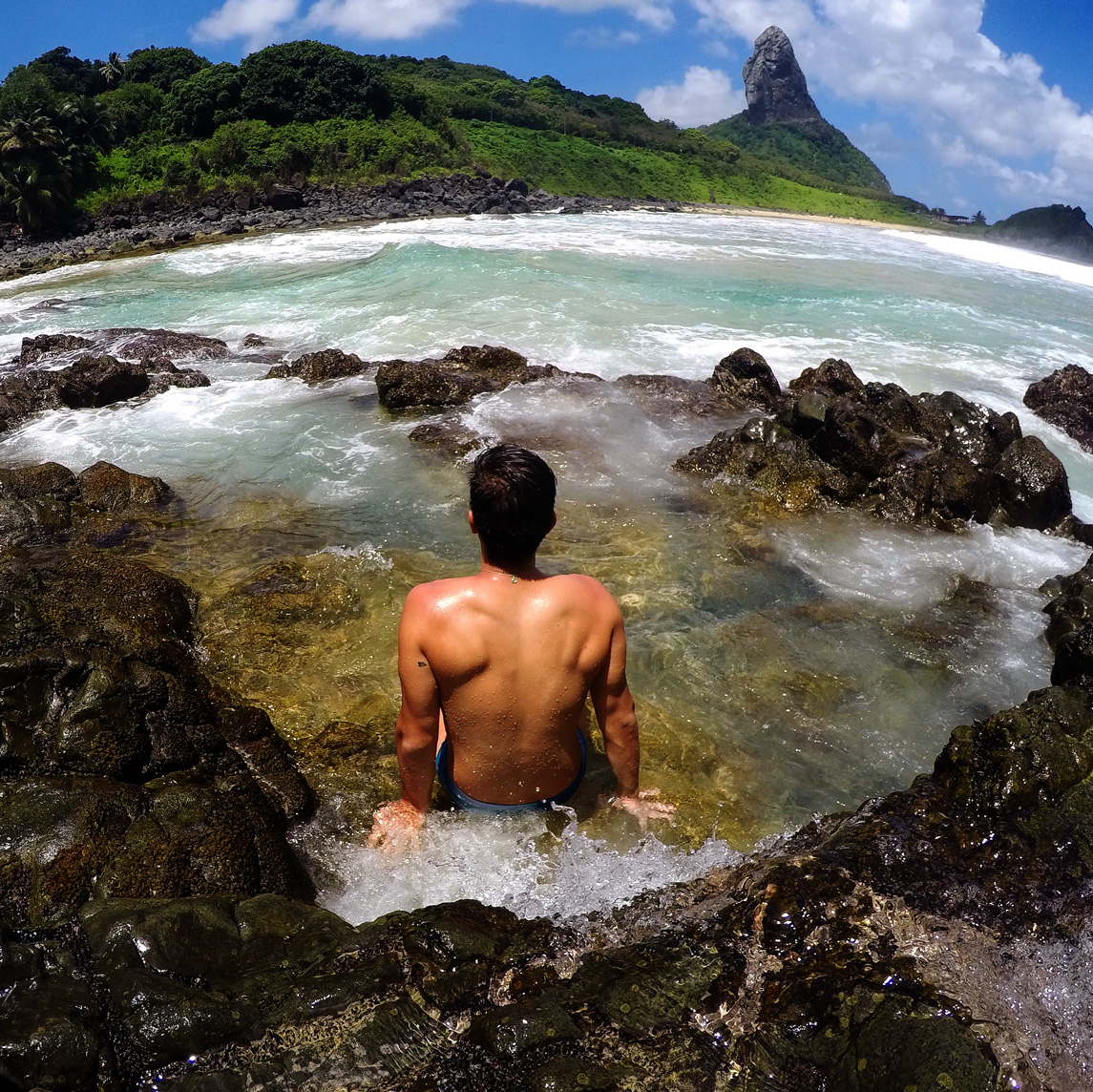 Rodrigo sentado nas rochas da Praia do Cachorro